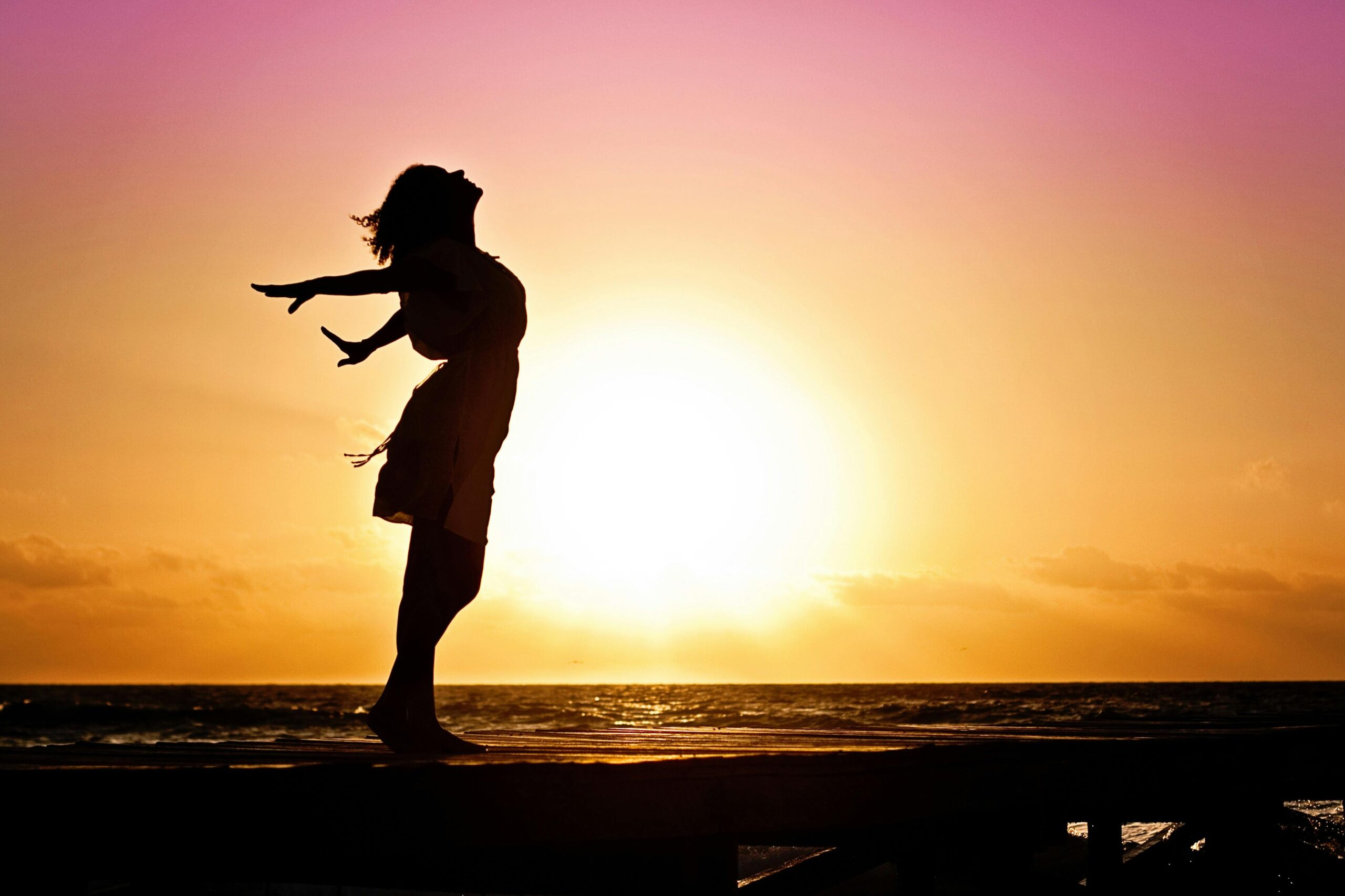 woman-happiness-sunrise-silhouette-40192-40192 Silhouette of a woman at the beach with arms outstretched against a vibrant sunset backdrop.