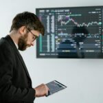 Professional man using tablet in front of cryptocurrency trading screen indoors.